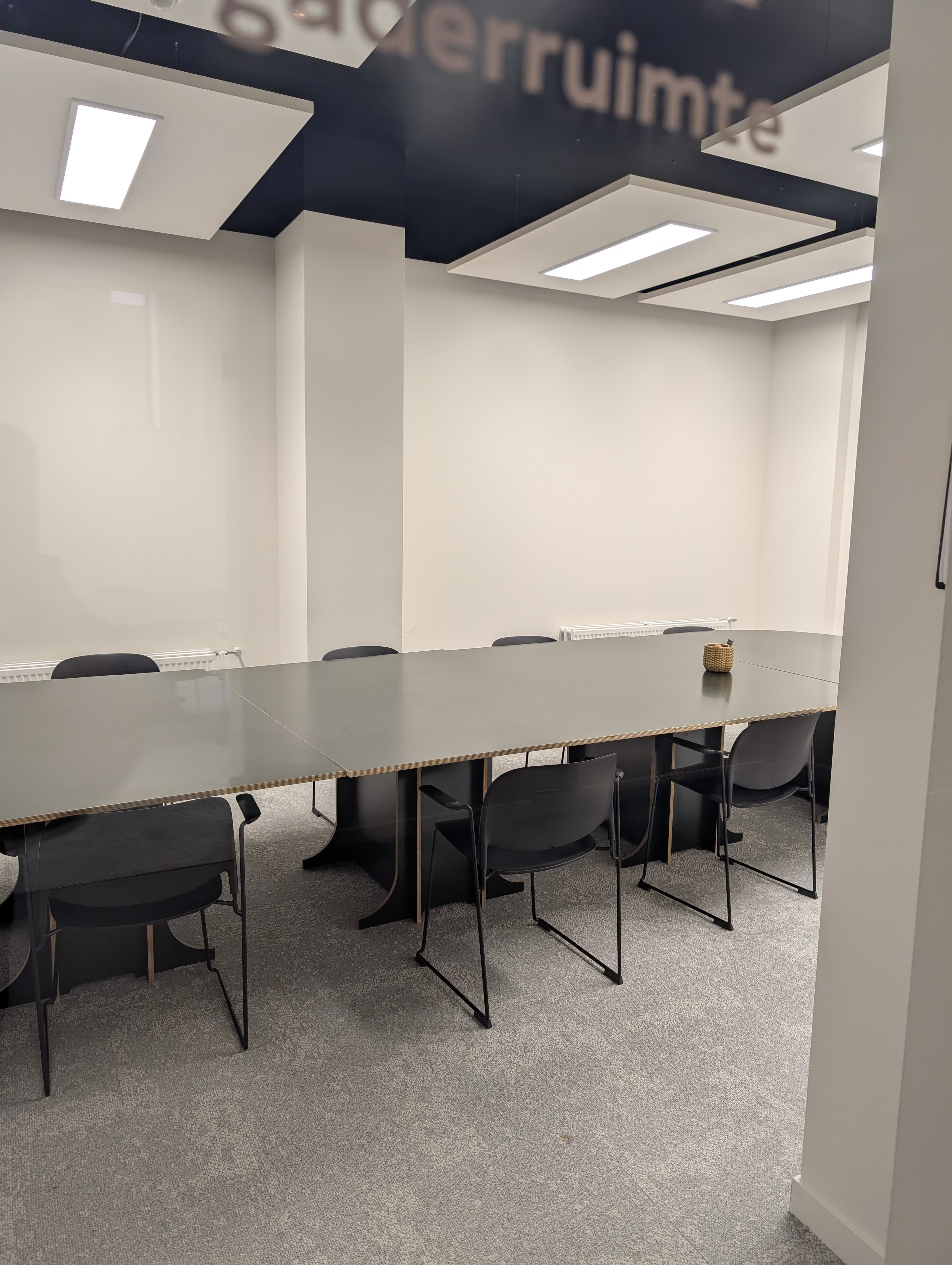 Lange vergadertafel met zwarte stoelen in vergaderkamer 1